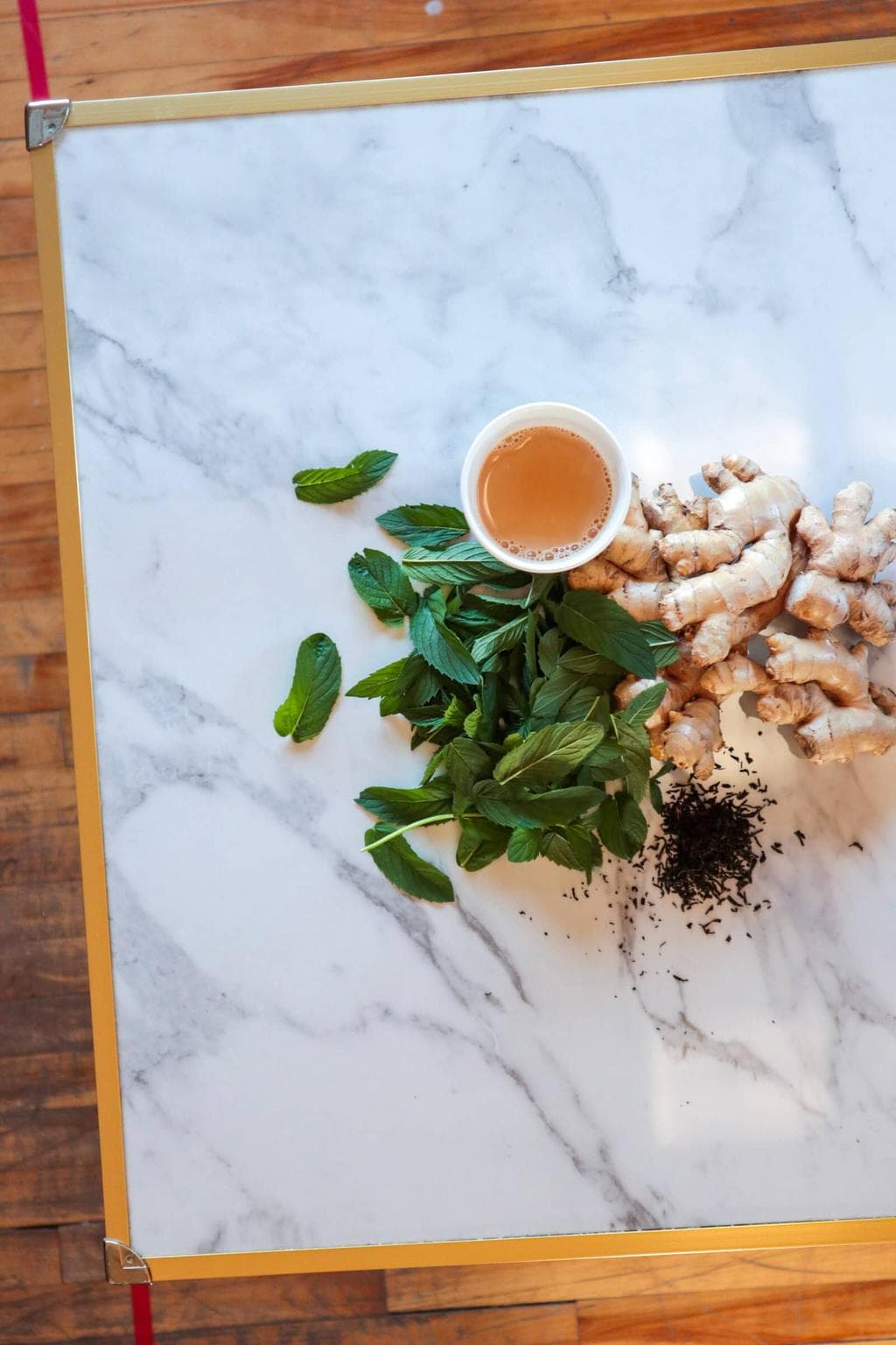 A cup of masala chai on a table with ingredients (ginger, tea and mint).